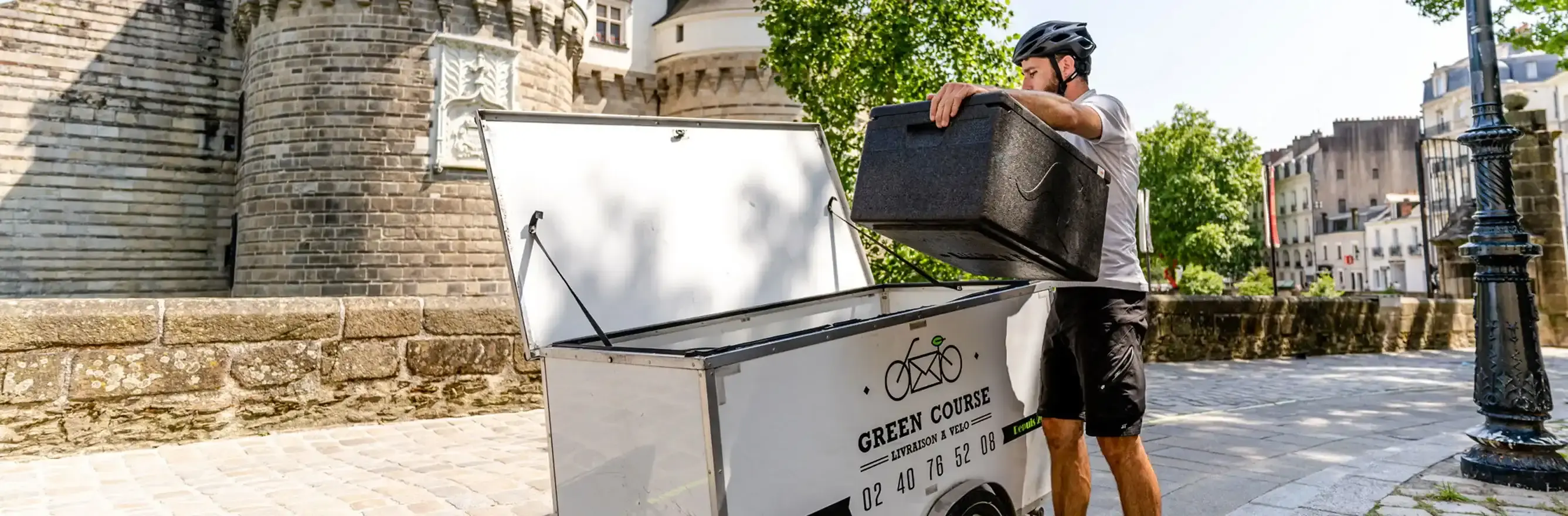 Livreur à vélo écologique charge une caisse isotherme noire devant le château des ducs de Nantes.