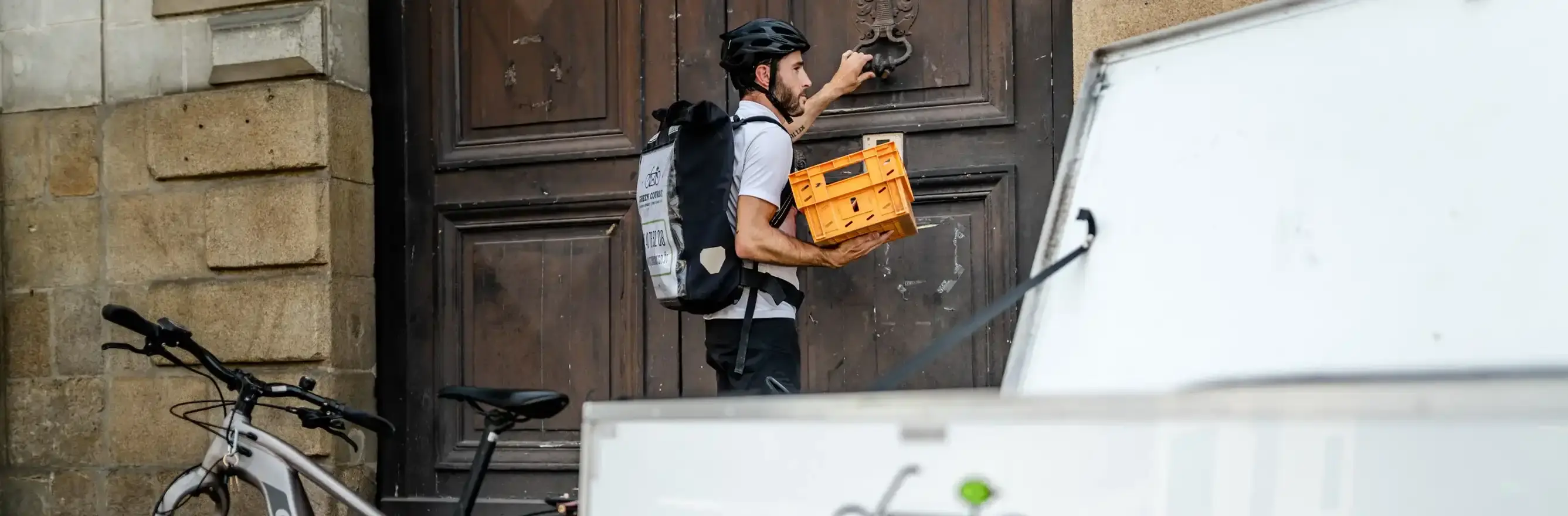 Coursier à vélo collectant du courrier ou des colis devant un bâtiment d'entreprise à Saint Herblain.