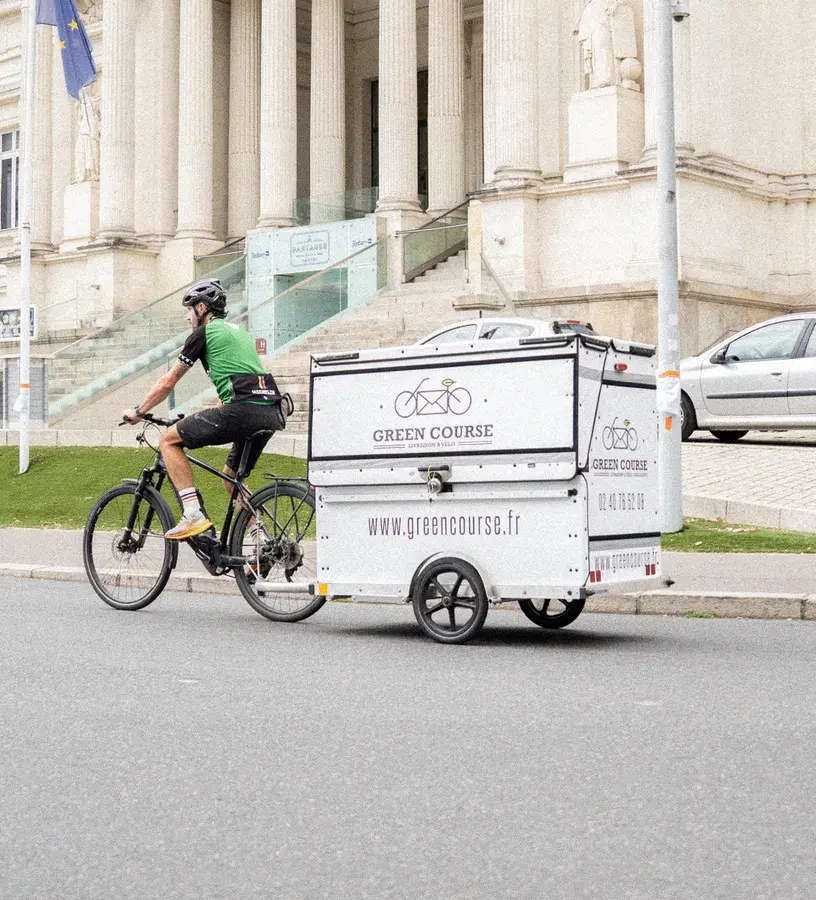 Livreur à vélo avec remorque Green Course passant devant le Radisson Blu de Nantes.