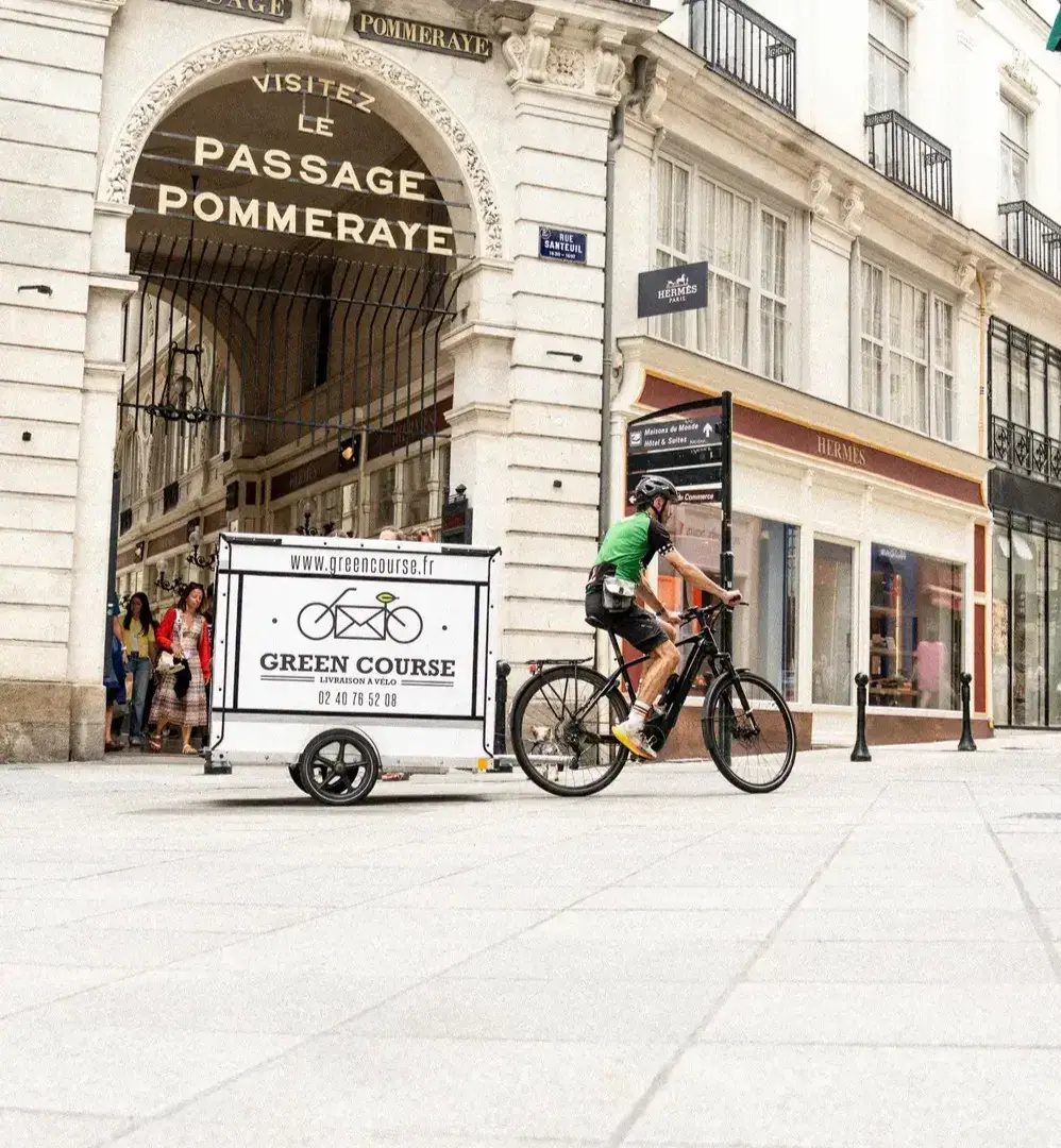 Livreur à vélo de l'entreprise Green Course avec sa remorque-caisson dans les rues de Nantes.