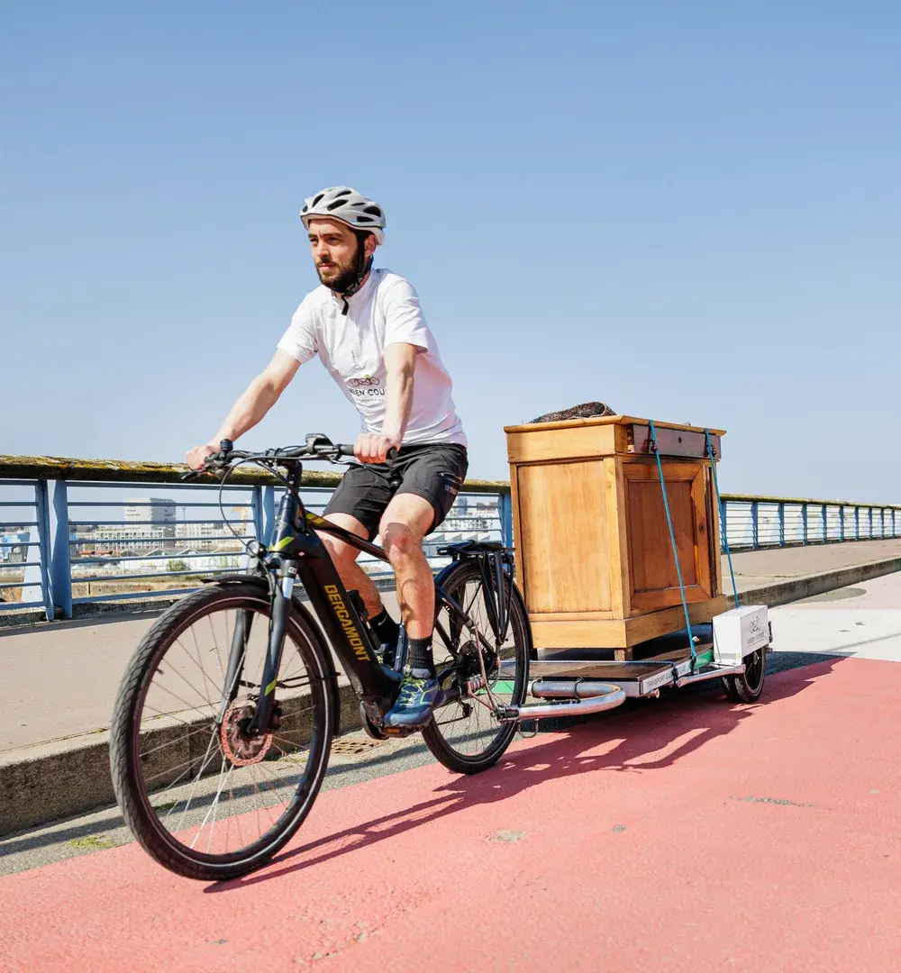Livreur à vélo transportant une commode sur sa remorque à vélo.